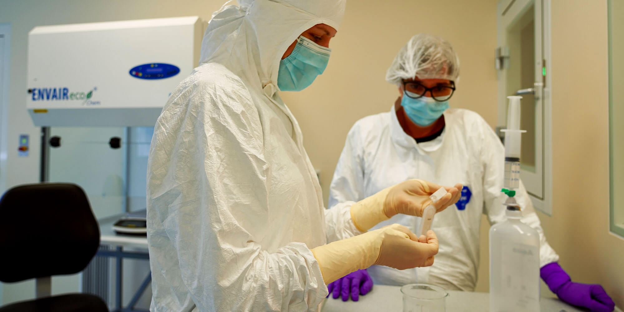 Zwei PTA im Reinraumlabor bei der sterilen Herstellung, mit Schutzkleidung, Maske und Handschuhen an Laborgeräten arbeitend.